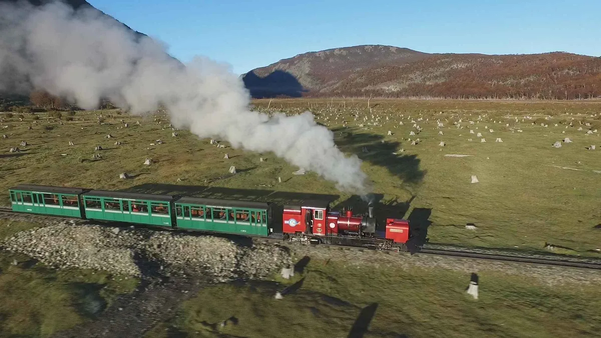 A red and white train carriage of the End of the World Train crossing a lenga forest valley in Tierra del Fuego National Park near Ushuaia, Argentina